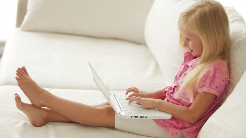 Cheerful little girl sitting on sofa using laptop and smiling