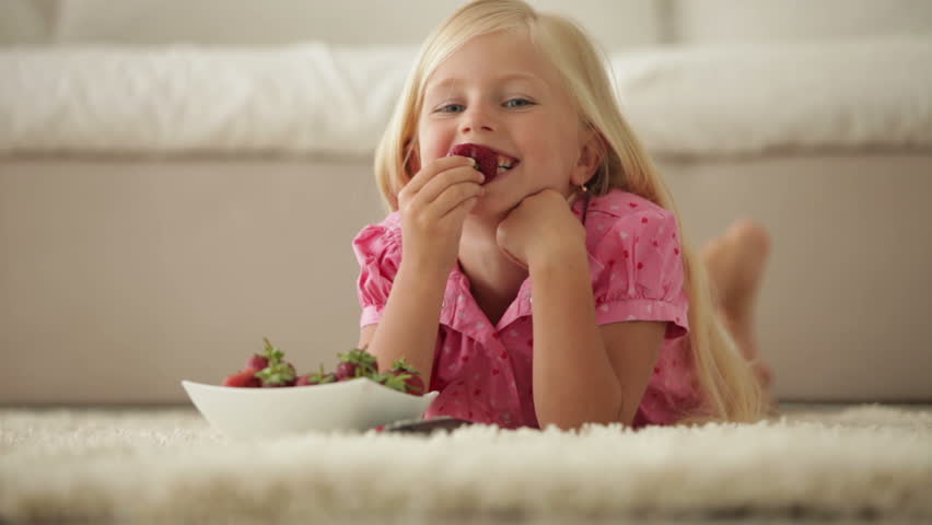 Cute little girl lying on floor eating strawberries and smiling