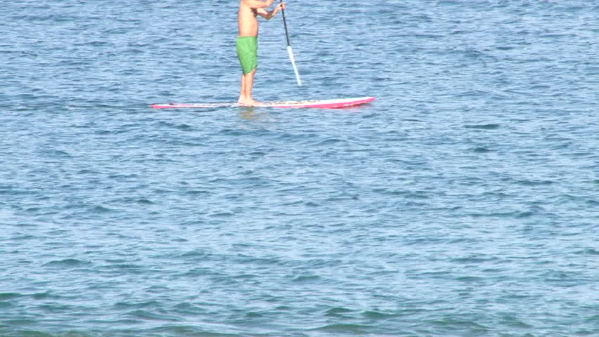 Unrecognizable man paddle boarding through frame.