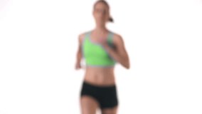 Medium shot of a female running in place on a treadmill, while looking into the camera on a white background