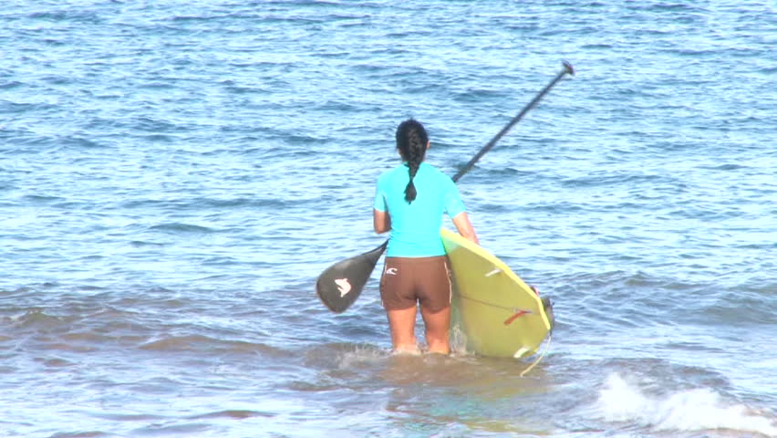 Woman enters ocean and paddle boards.