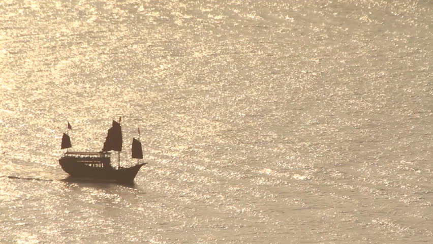 Chinese traditional sailing junk silhouetted cruising in the ocean during sunset
