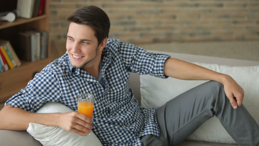 Attractive young man relaxing on sofa drinking juice and smiling