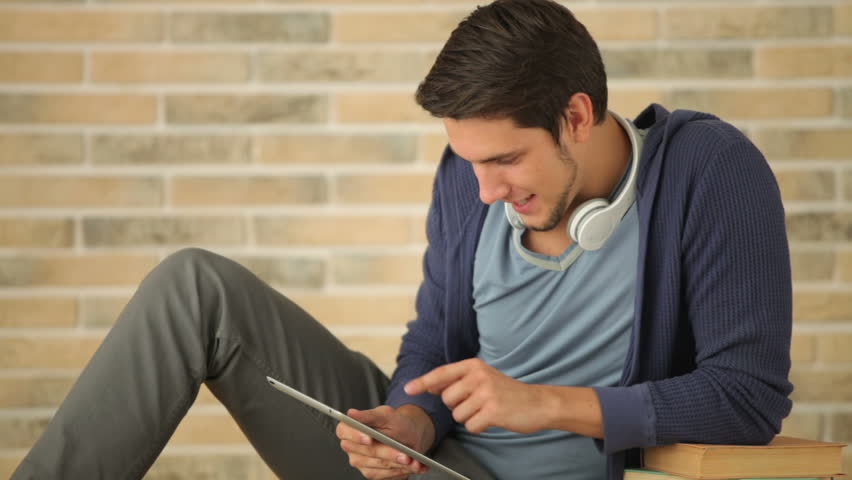 Charming guy in headset sitting on floor with books and using touchpad