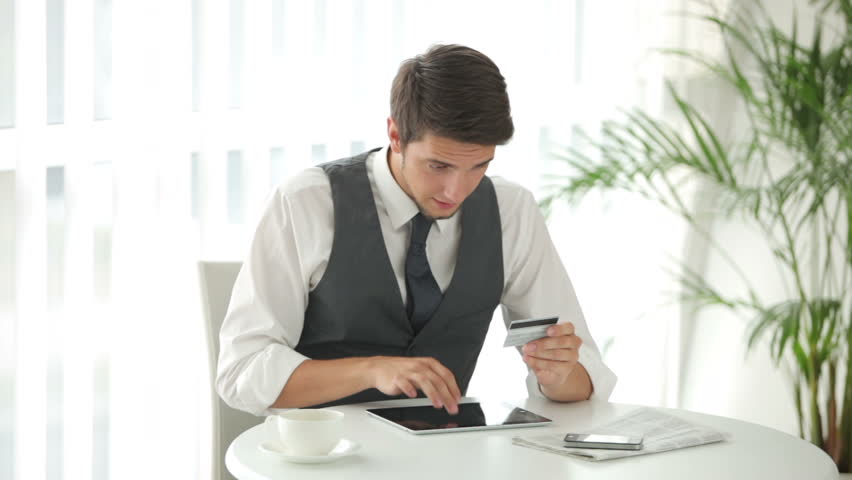 Attractive young man sitting at table with touchpad and holding credit card