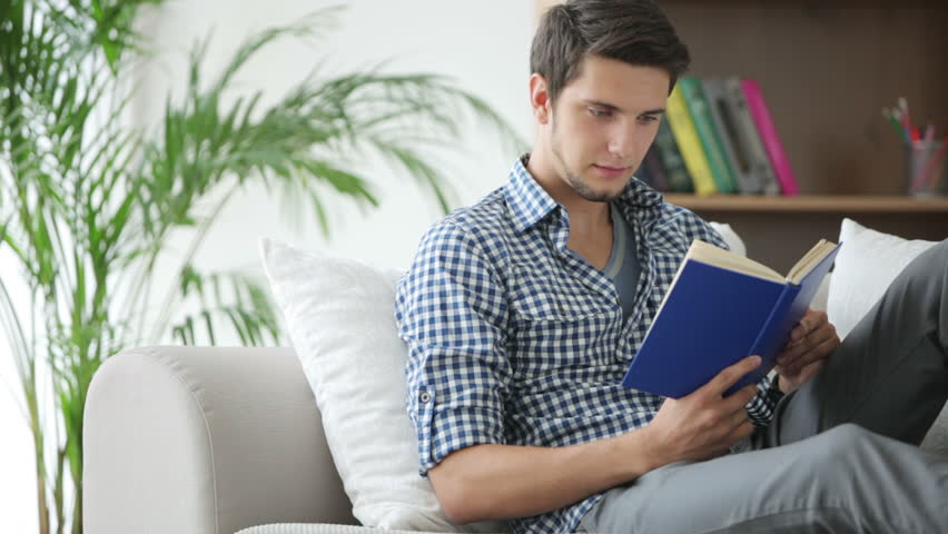 Attractive young man sitting on couch and reading book