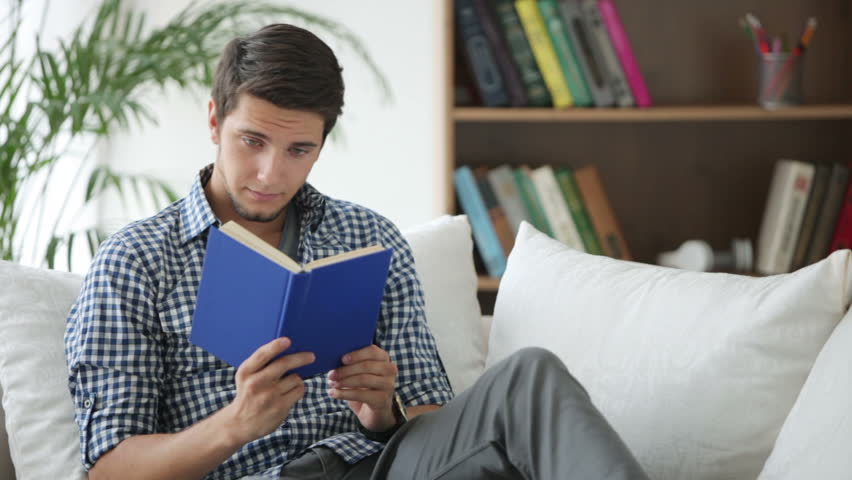 Attractive guy sitting on sofa reading book and closing it