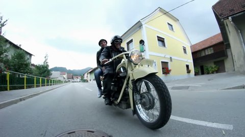 Middle aged couple driving on old motorcycle in small town