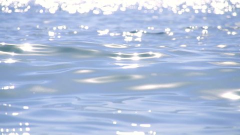 Sparkling fresh wavy water is shining on a sunny summer day in slow motion, abstract blurry background at the seaside