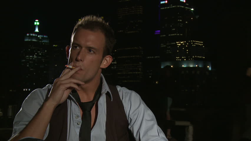 Young man enjoying a cigarette with the city of Toronto lit up behind him.