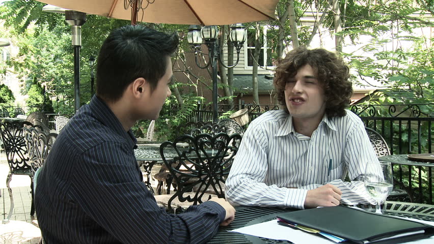 Two young men shake hands and start a business discussion at an outdoor cafe or