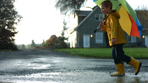 Young boy running through puddles with umbrella, slow motion