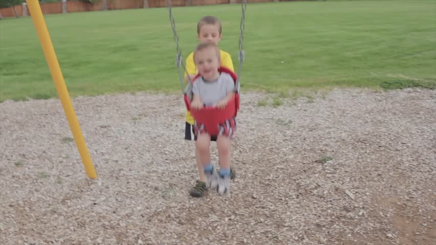 A brother pushing his baby brother on the swings at the park