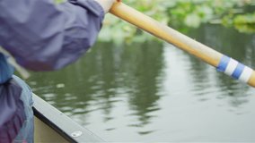 A woman sits in a boat and uses a paddle to move through the river. Close up shot.