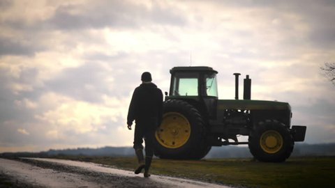 A farmer walks towards his tractor in the early morning while silhouetted 