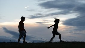 Happy children running, jumping and playing on meadow, silhouettes at summer sunset