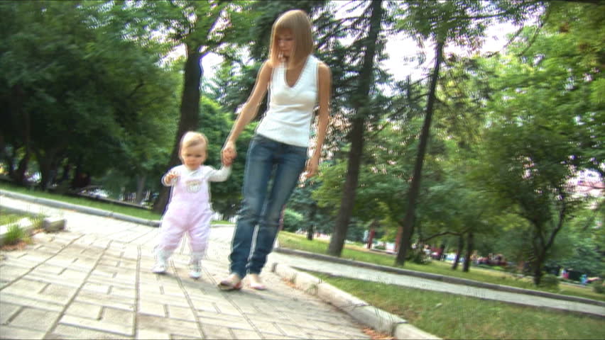 9 month old girl walks toward camera with help of her mother.
