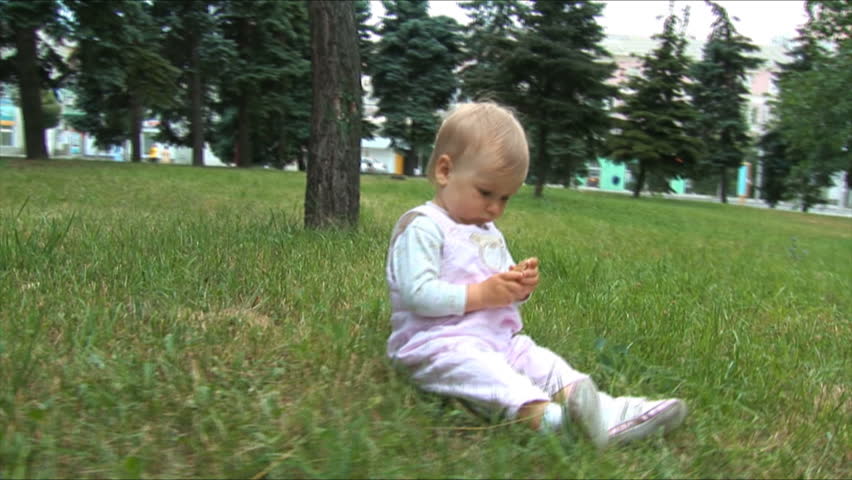 Little baby sits in a grass and holds a pine cone. 