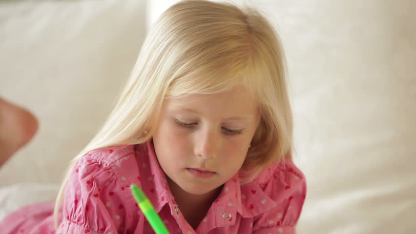 Funny little girl lying on sofa writing in notebook and smiling