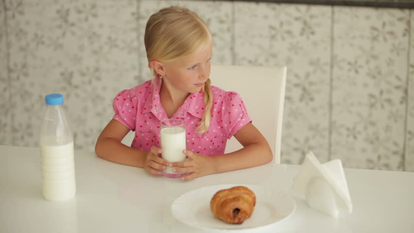 Funny little girl sitting at kitchen table drinking milk and smiling