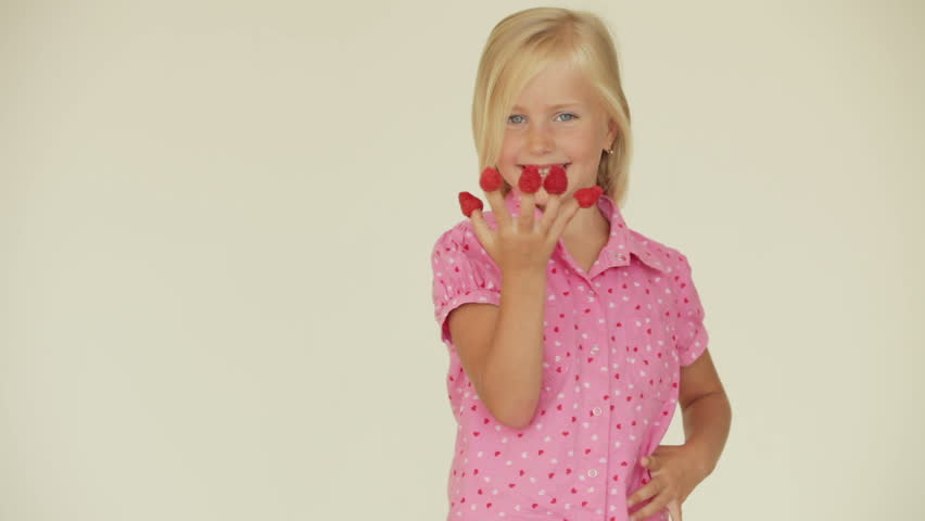 Funny little girl posing with raspberries on her fingers and showing thumb up
