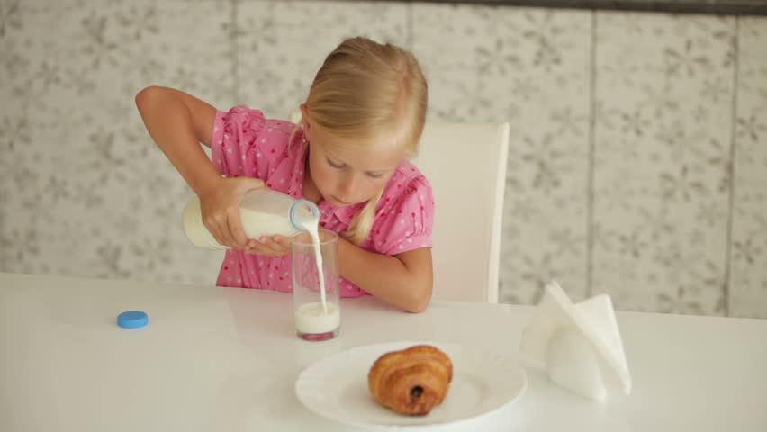 Cute little girl sitting at kitchen table and pouring milk into glass