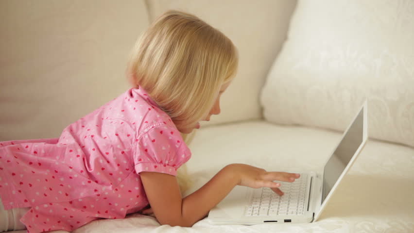 Cute little girl lying on sofa using laptop and smiling