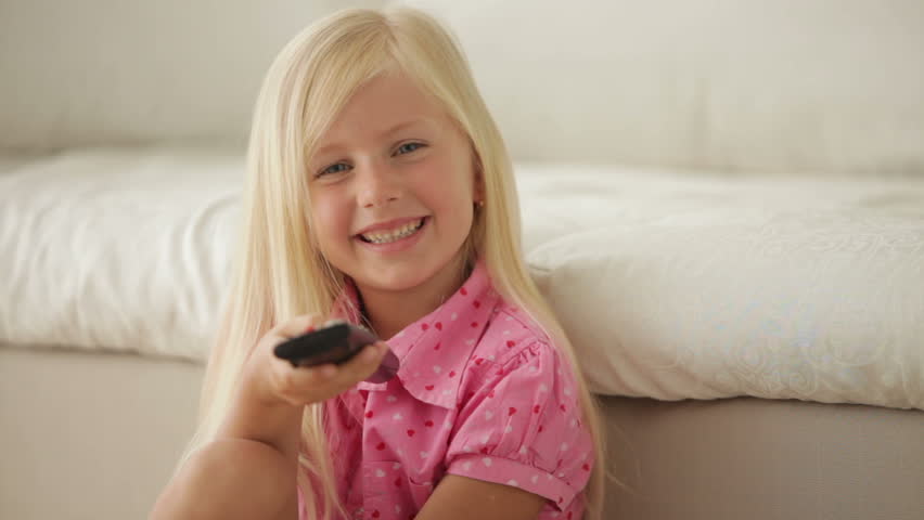 Funny little girl holding remote control smiling and showing thumb up