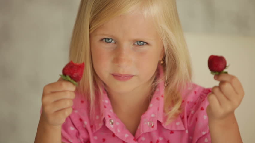 Funny little girl eating strawberries and smiling