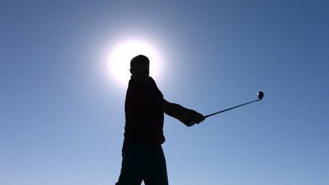 Silhouette of golfer teeing off, slow motion
