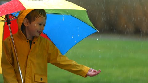 Young boy in rain with umbrella, slow motion