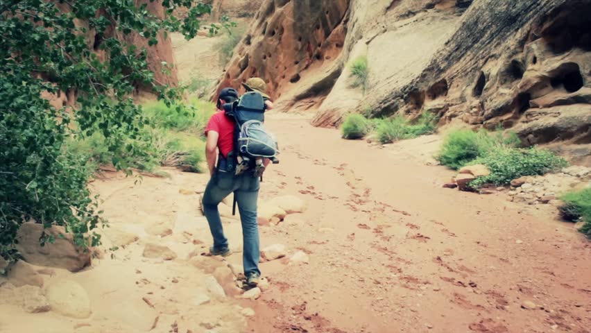 A father carrying his baby through a desert slot canyon in a backpack carrier