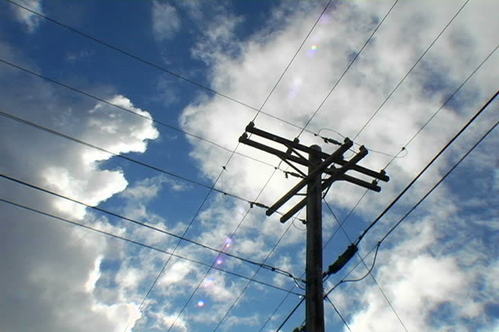 Low angle on utility pole, with dramatic clouds moving across a blue sky above.