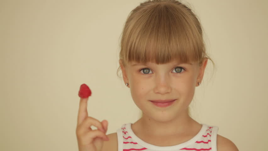 Little girl eating raspberries from top of her fingers and showing thumb up
