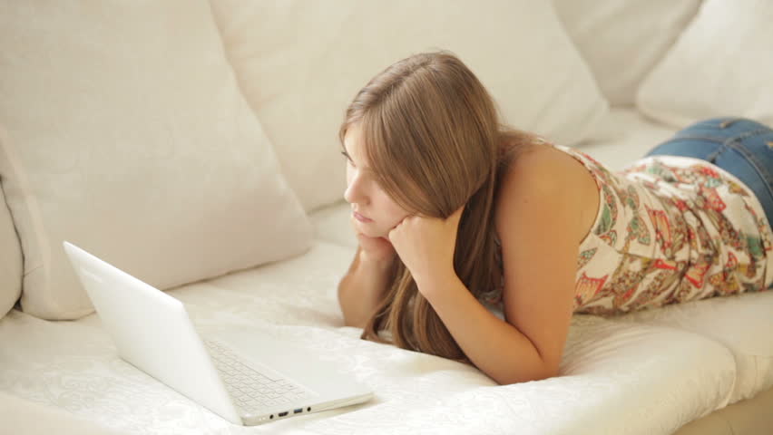 Young woman lying on sofa and using laptop