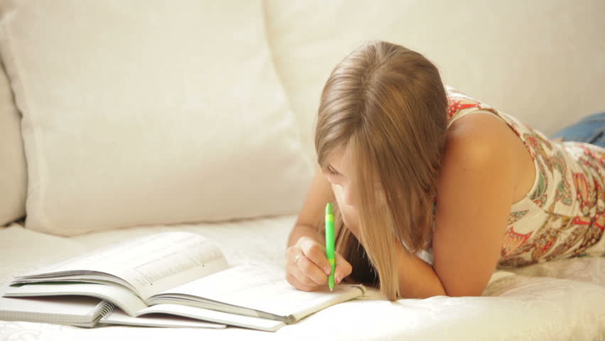 Student girl lying on sofa writing in notebook and smiling