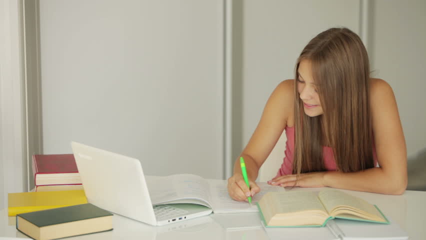 Student girl sitting at table and writing in notebook