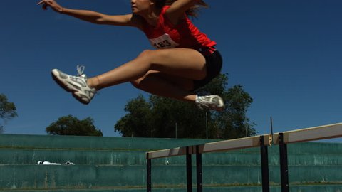 Track athlete jumps over hurdle, slow motion