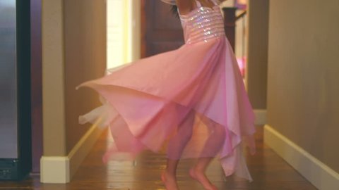 A little girl is dressed up in a ballerina costume dances through the hallway. Medium slow motion dolly shot.