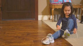 This video has two clips in it, in one a cute little girl tries to tie her shoe alone, int he other her mom pops in and helps to tie it. Two clips put together. Slow motion medium shot.