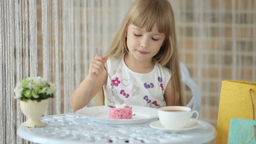 Cute little girl sitting at table eating cake smiling and showing thumb up at