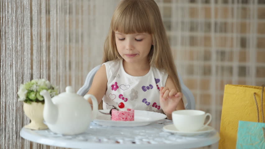 Pretty little girl sitting at cafe eating cake and smiling at camera