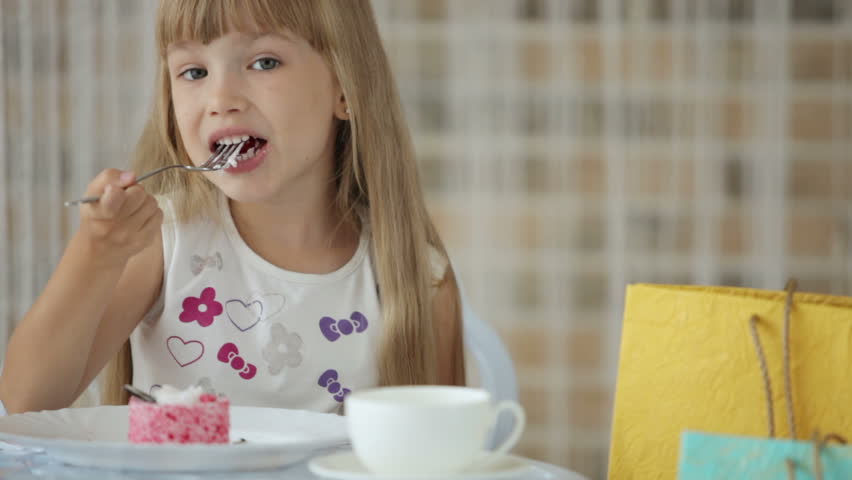 Charming little girl sitting at cafe eating cake and smiling at camera