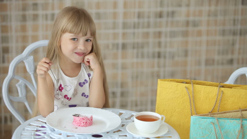 Little girl sitting at cafe eating cake and smiling at camera