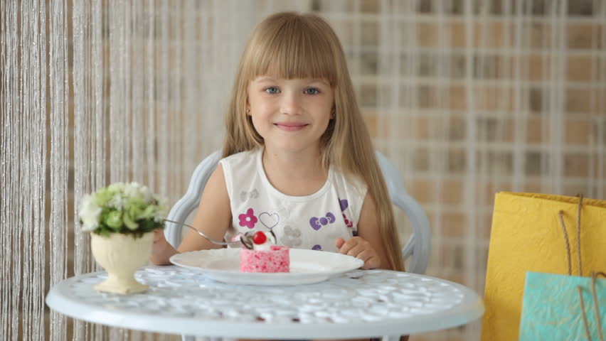 Cute little girl sitting at cafe eating cake and smiling at camera