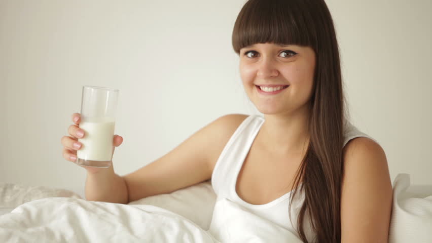 Happy girl relaxing in bed drinking milk and smiling at camera