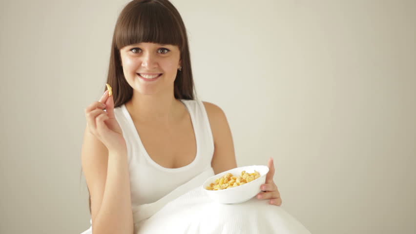Pretty girl sitting on bed eating cereal and smiling at camera