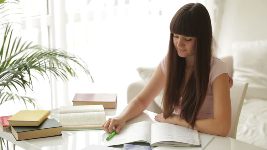 Student girl studying at table writing in notebook and smiling