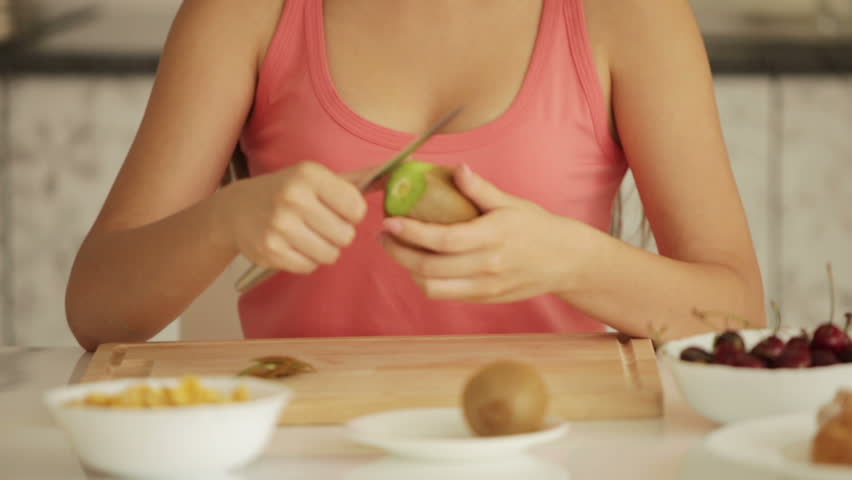 Pretty girl sitting at kitchen table and peeling kiwi