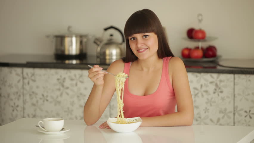 Young woman sitting at table eating noodle and smiling